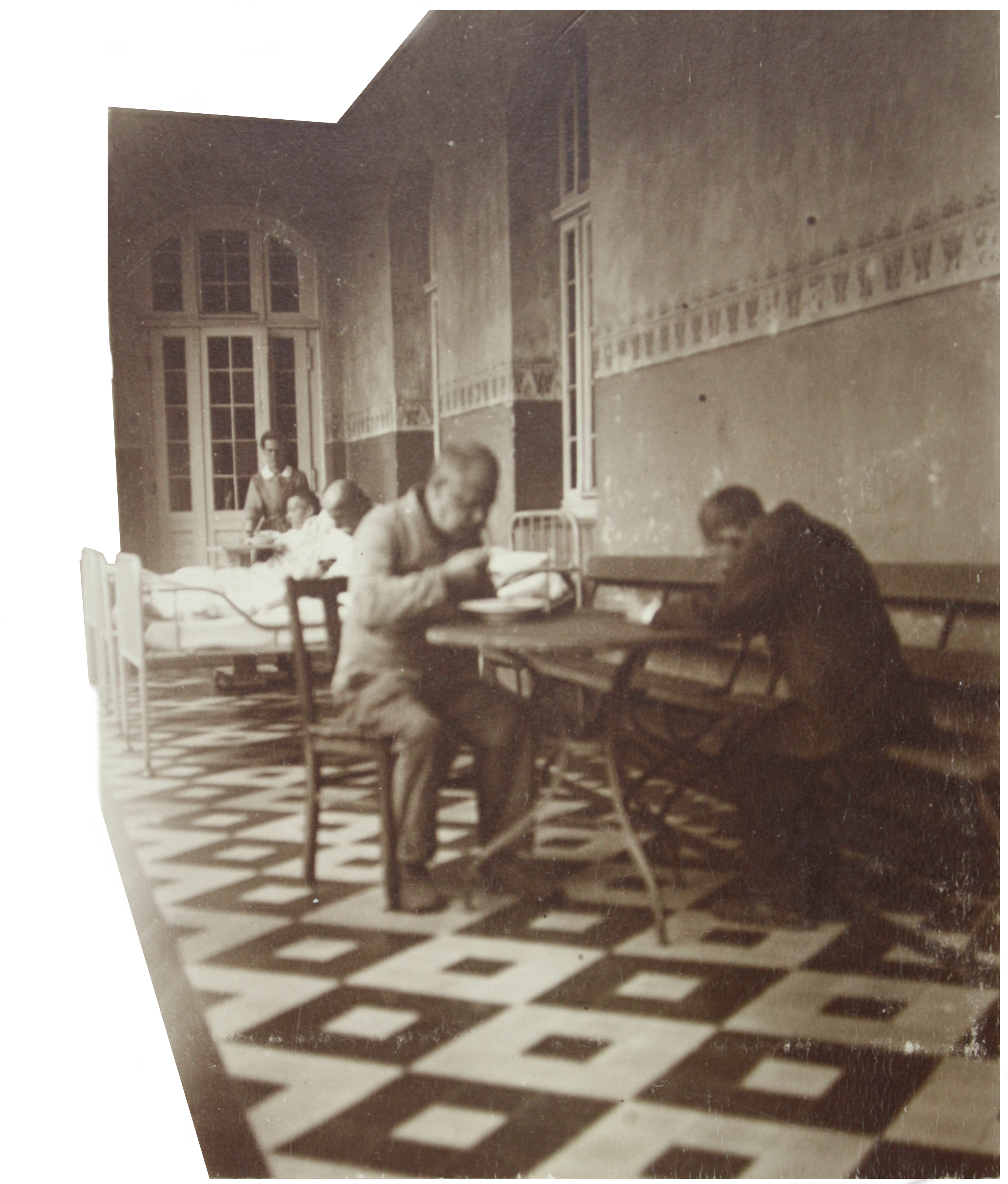 Schwarzweiß Foto zweier Männer, die an einem Tisch sitzen, im Hintergrund ein Krankenbett.